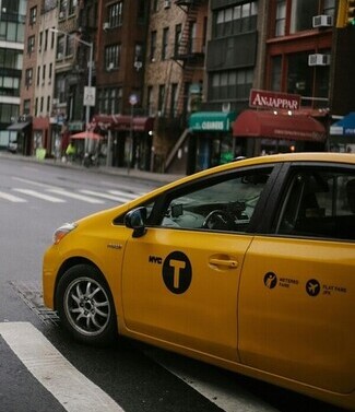 Iconic yellow taxi navigating a New York City street with historic buildings.